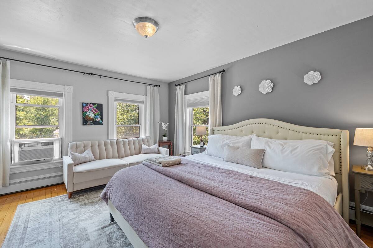 A bedroom with a large bed, a sofa, and a window with a view.