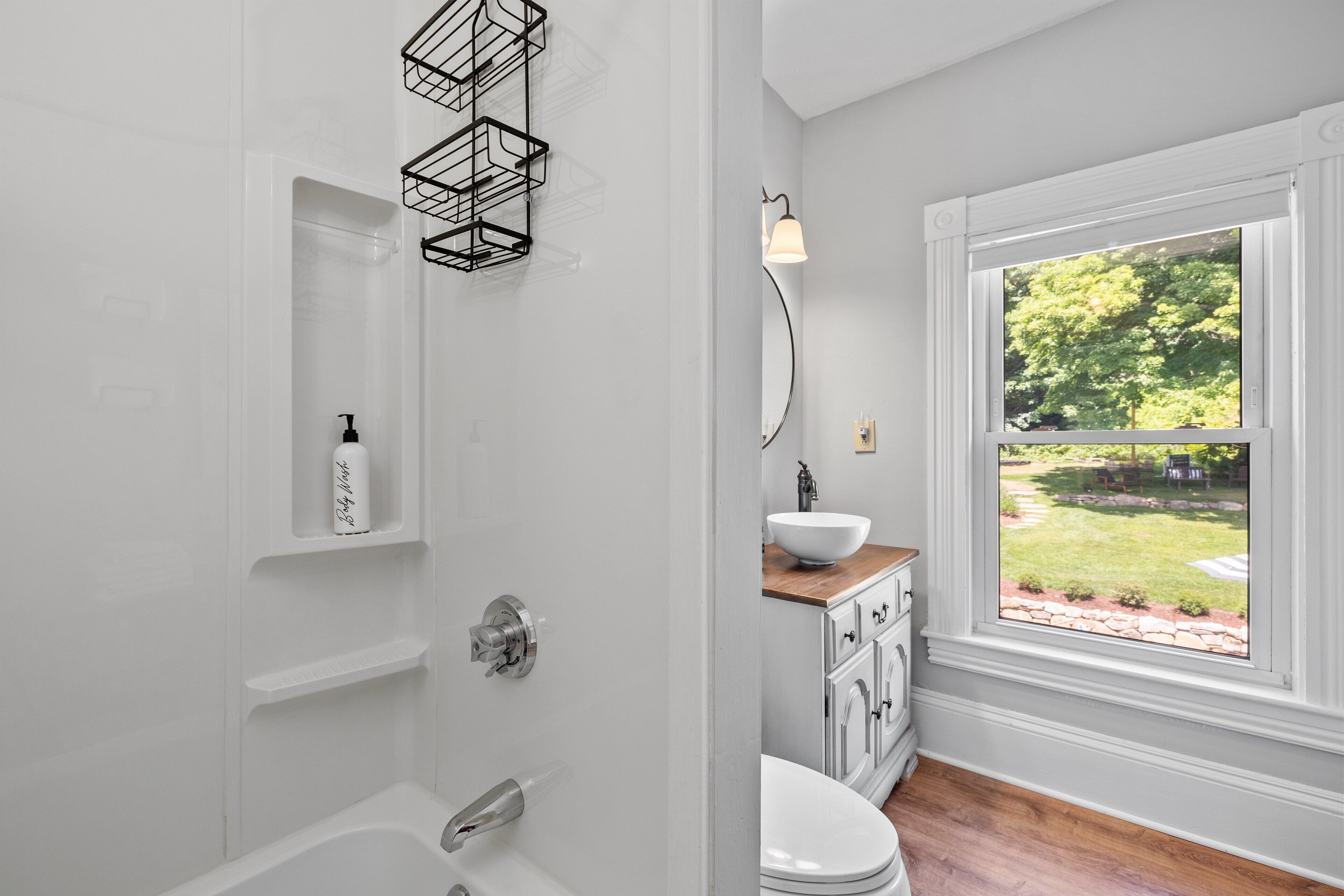 A bathroom with a bathtub, a toilet, a sink, and a window with a view of a garden.