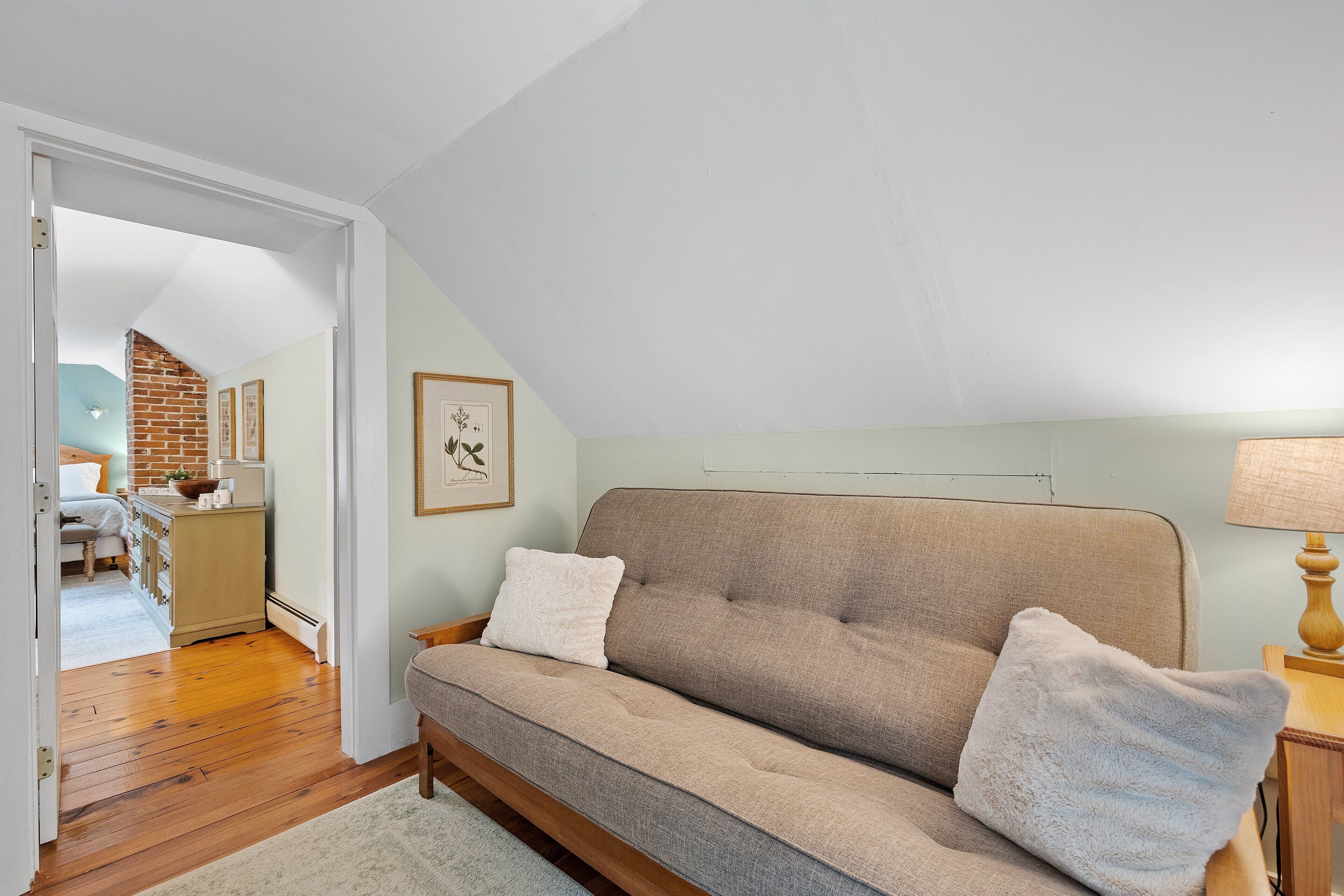 A cozy room with a beige sofa, a wooden floor, and a kitchen in the background.