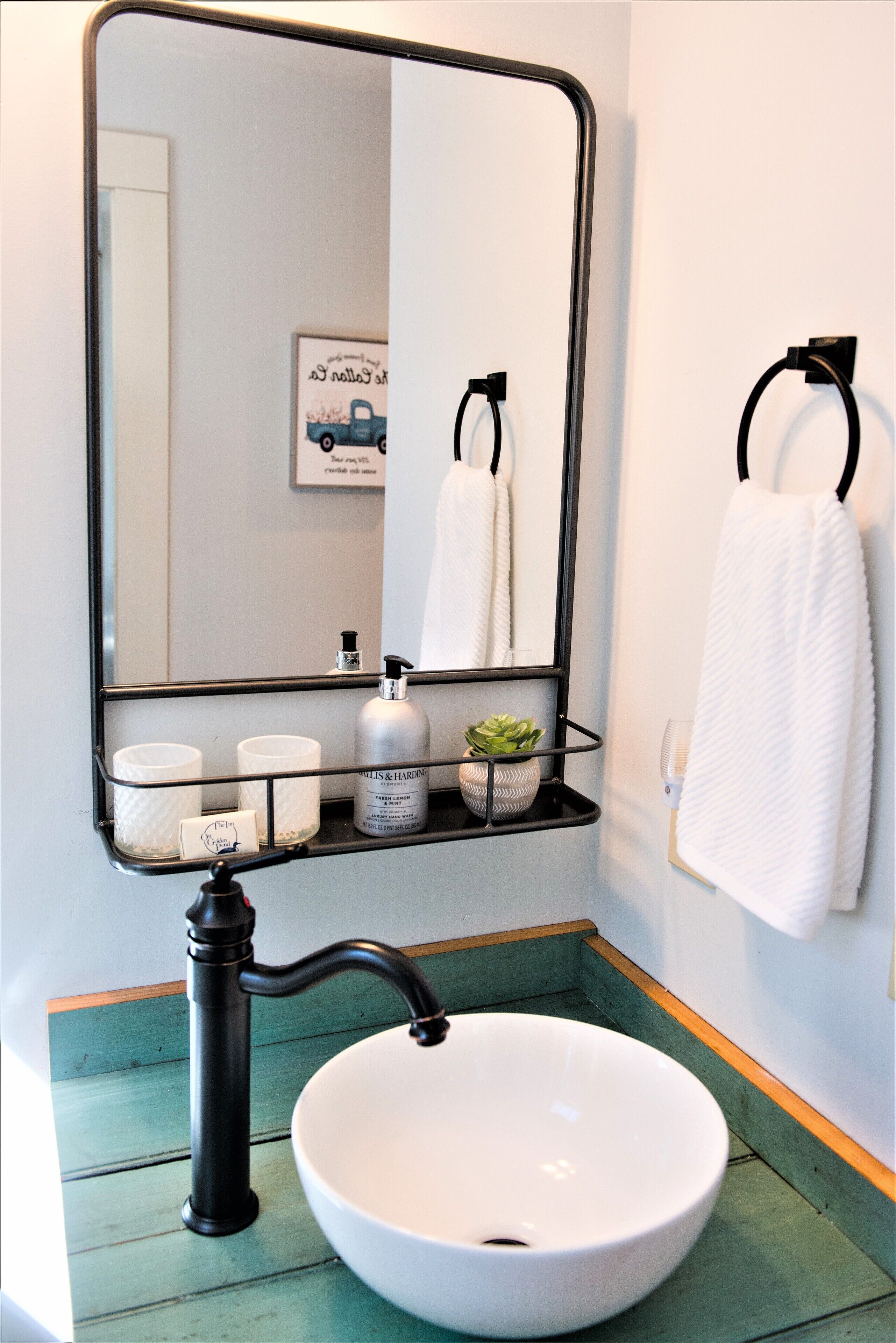 A bathroom with a white sink, black faucet, and a mirror above it. There are toiletries on a shelf below the mirror.