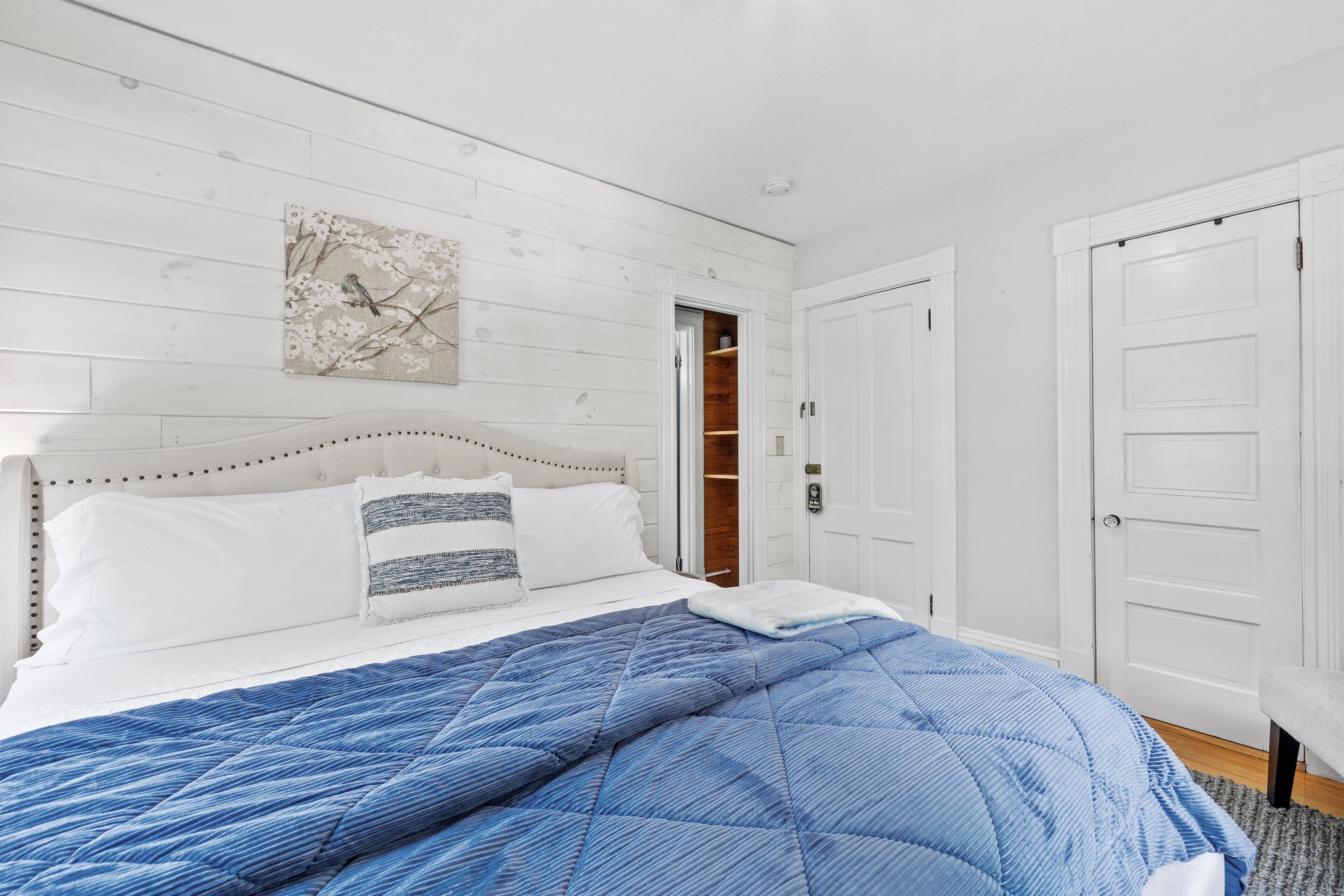 A bedroom with a bed, a white door, and a wooden wall.