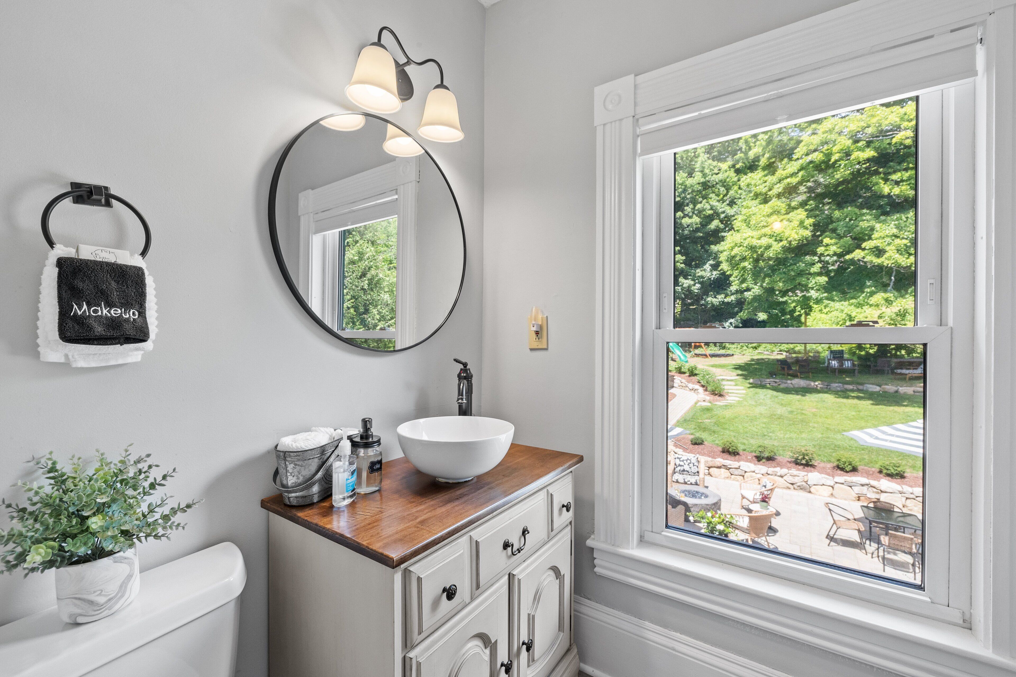 A bathroom with a white sink, wooden countertop, and a large window with a view of a garden.