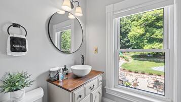 A bathroom with a white sink, wooden countertop, and a large window with a view of a garden.