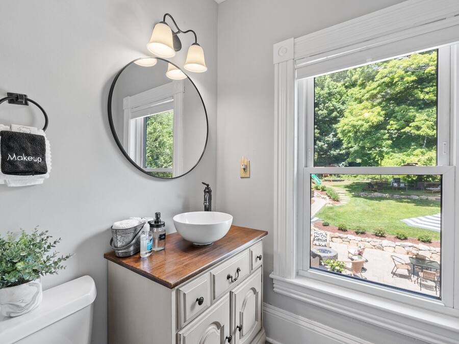 A bathroom with a white sink, wooden countertop, and a large window with a view of a garden.