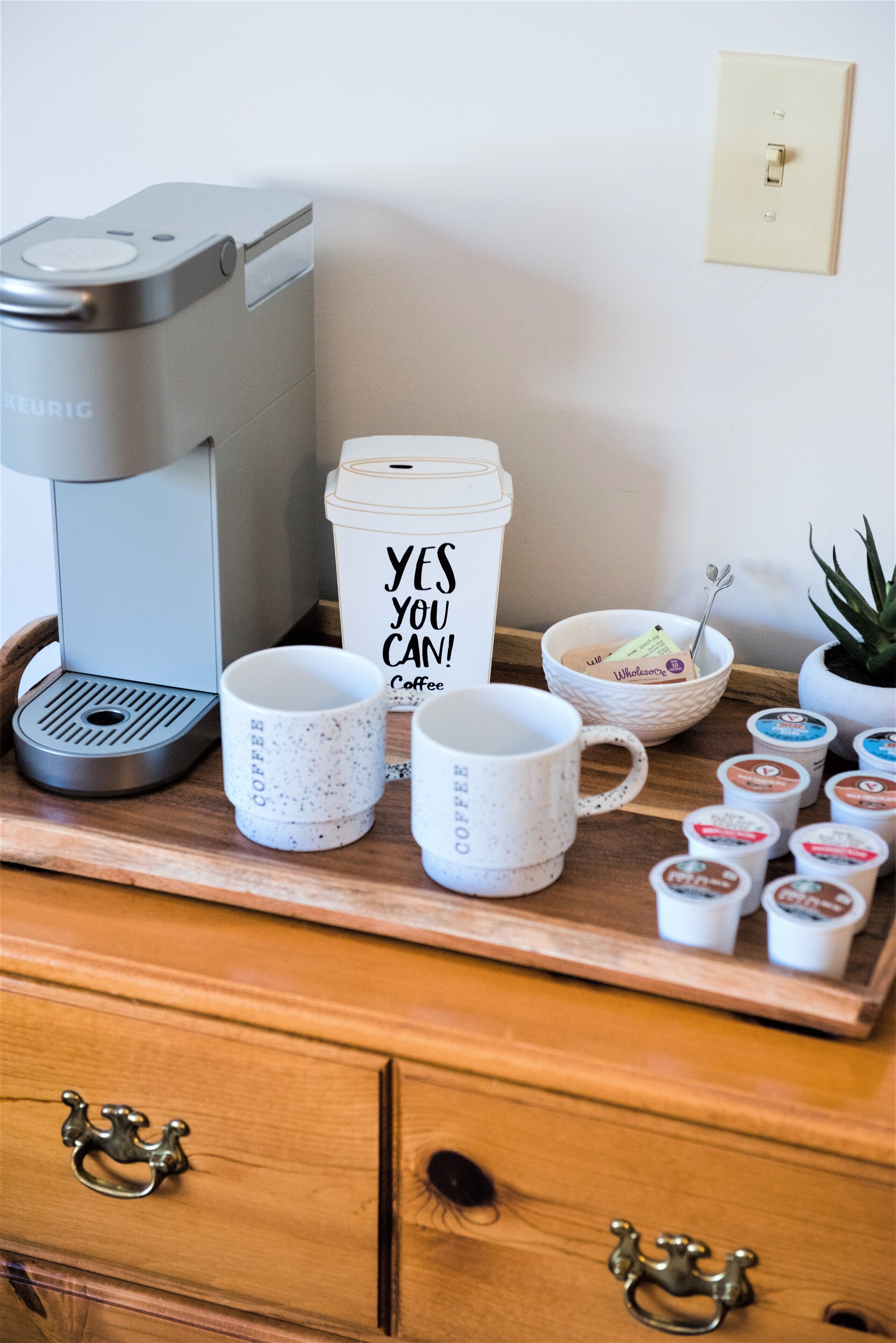 Una estación de café con una cafetera Keurig, una taza blanca grande con la inscripción 