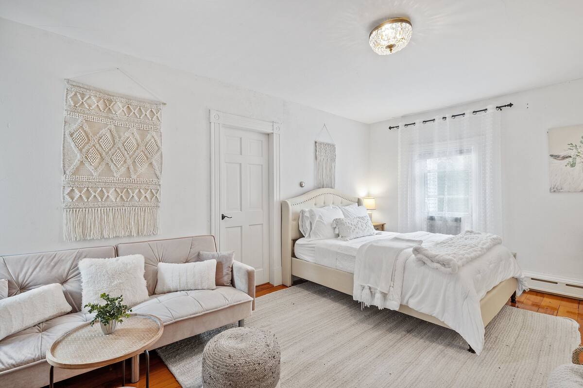A bedroom with a bed, a sofa, a small round table, and a wall hanging.