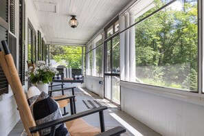 Eine überdachte Veranda mit Holzbänken, einem Topfpflanzen und Blick auf Grünflächen.