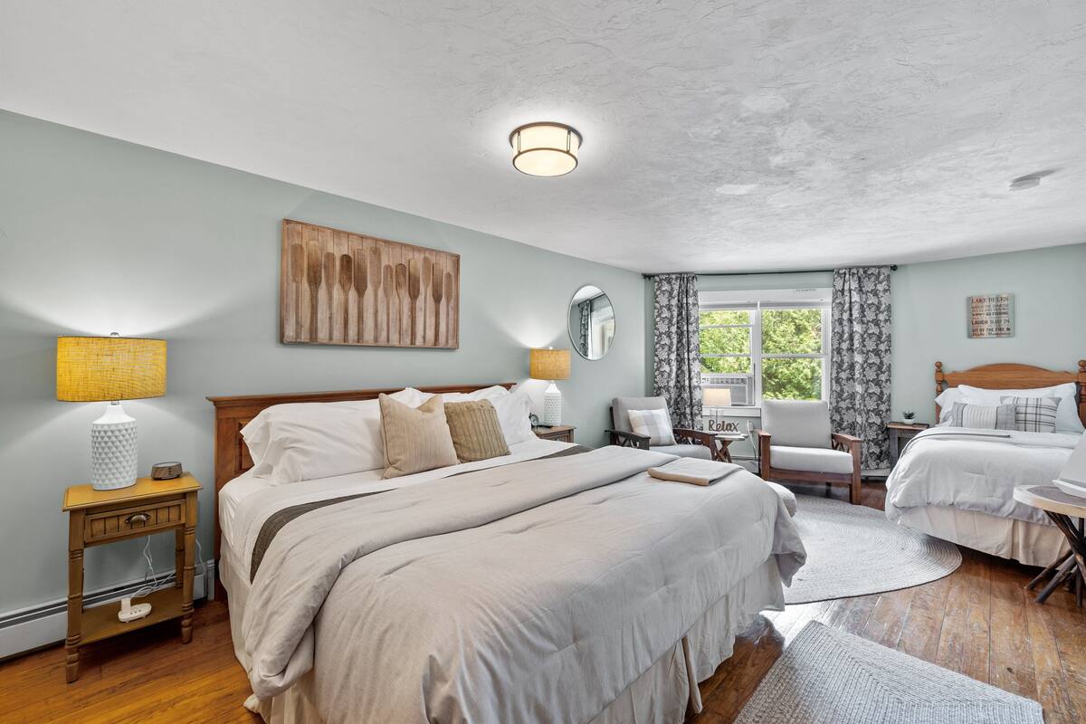 A bedroom with a large bed, two bedside tables, a chair, a desk, and a window with curtains.