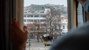 Une vue à travers une fenêtre avec des rideaux, mettant en scène un bâtiment avec une colline imposante en arrière-plan.