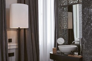 Ένα μοντέρνο μπάνιο με έναν μεγάλο καθρέφτη, έναν λευκό εντοιχιζόμενο νιπτήρα και ένα φωτιστικό δαπέδου.