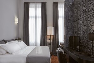A hotel room with a bed, a desk, a TV, and a lamp.