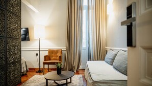 Une chambre d’hôtel moderne, équipée d’un canapé, d’un fauteuil, d’une petite table avec une plante, d’une lampe et d’un panneau décoratif mural.