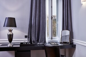 Ett rum med ett skrivbord, en lampa, en spegel och ett fönster med gardiner.
