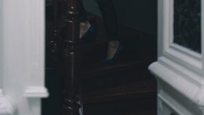 Une personne descend un escalier en bois, dont l’intérieur est sombre et les éléments de finition sont blancs.