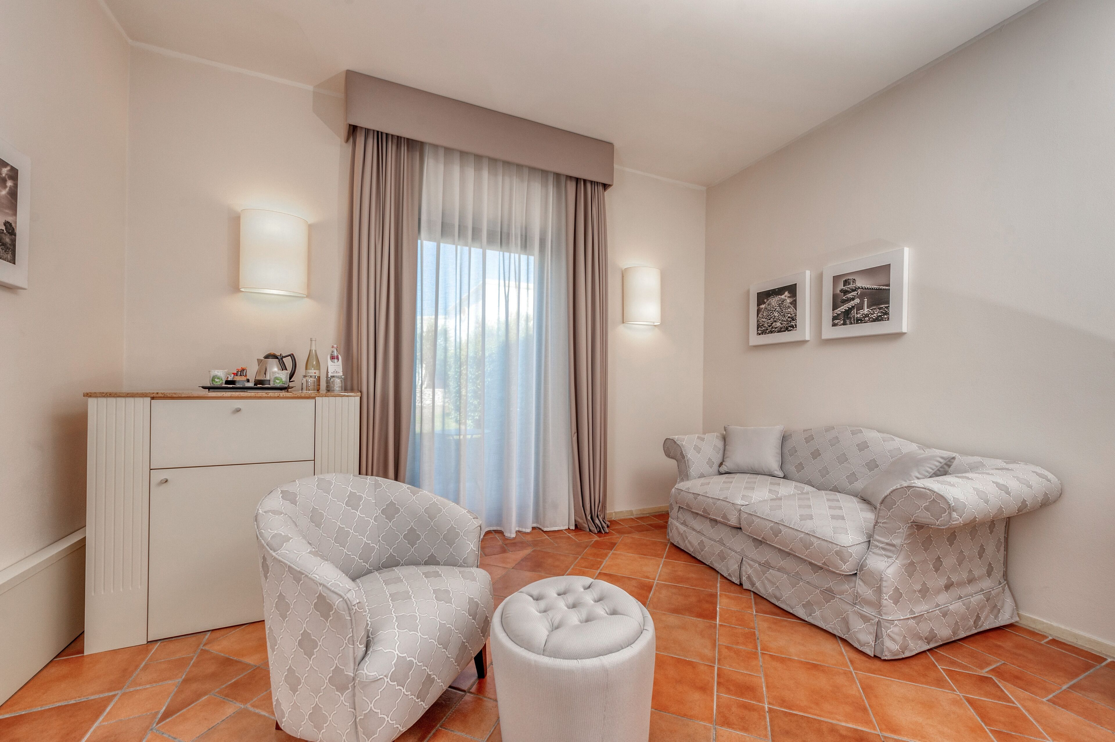Sala de estar moderna com sofá, poltrona, banquinho e pequena área de cozinha.