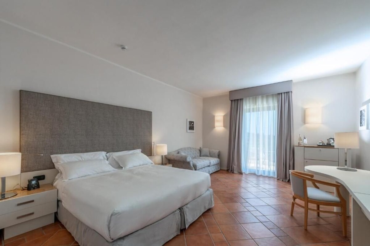 A hotel room with a large bed, a desk, a chair, and a small sofa.