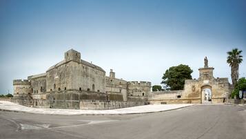 A historic stone building with a large central tower, a fortified entrance, and a palm tree in the background.