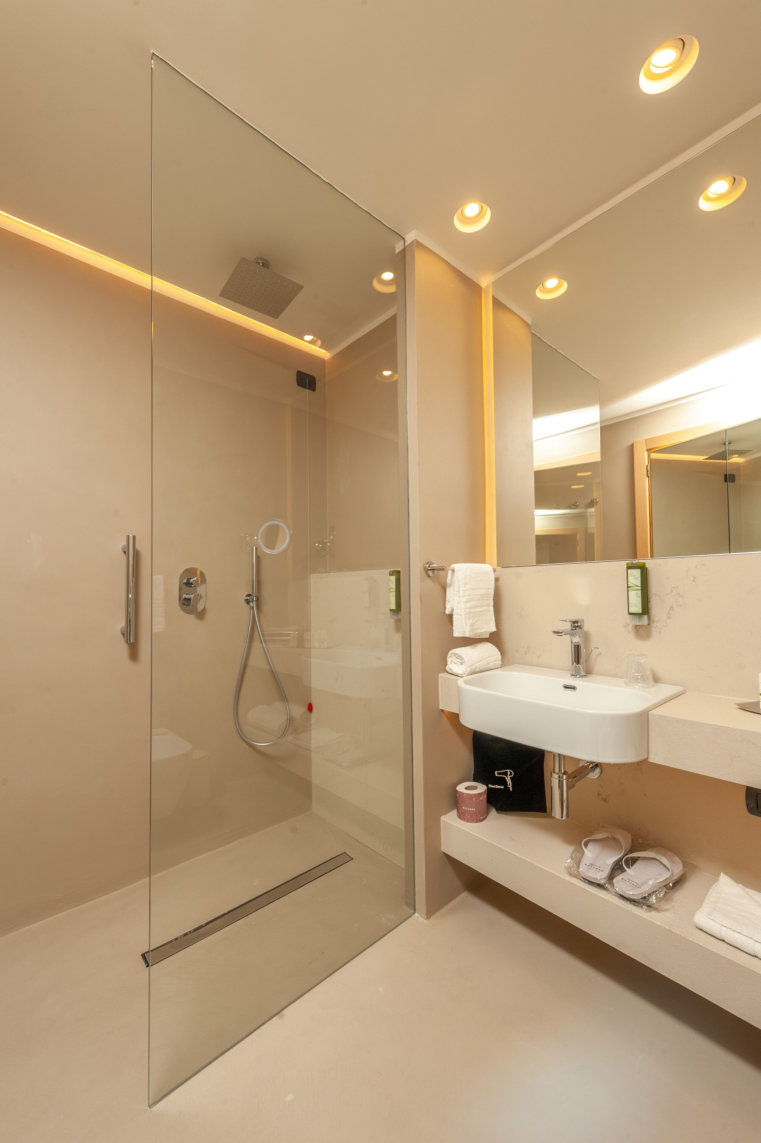 Ein modernes Badezimmer mit einer gläsernen Dusche, einem weißen Waschbecken und einem großen Spiegel.