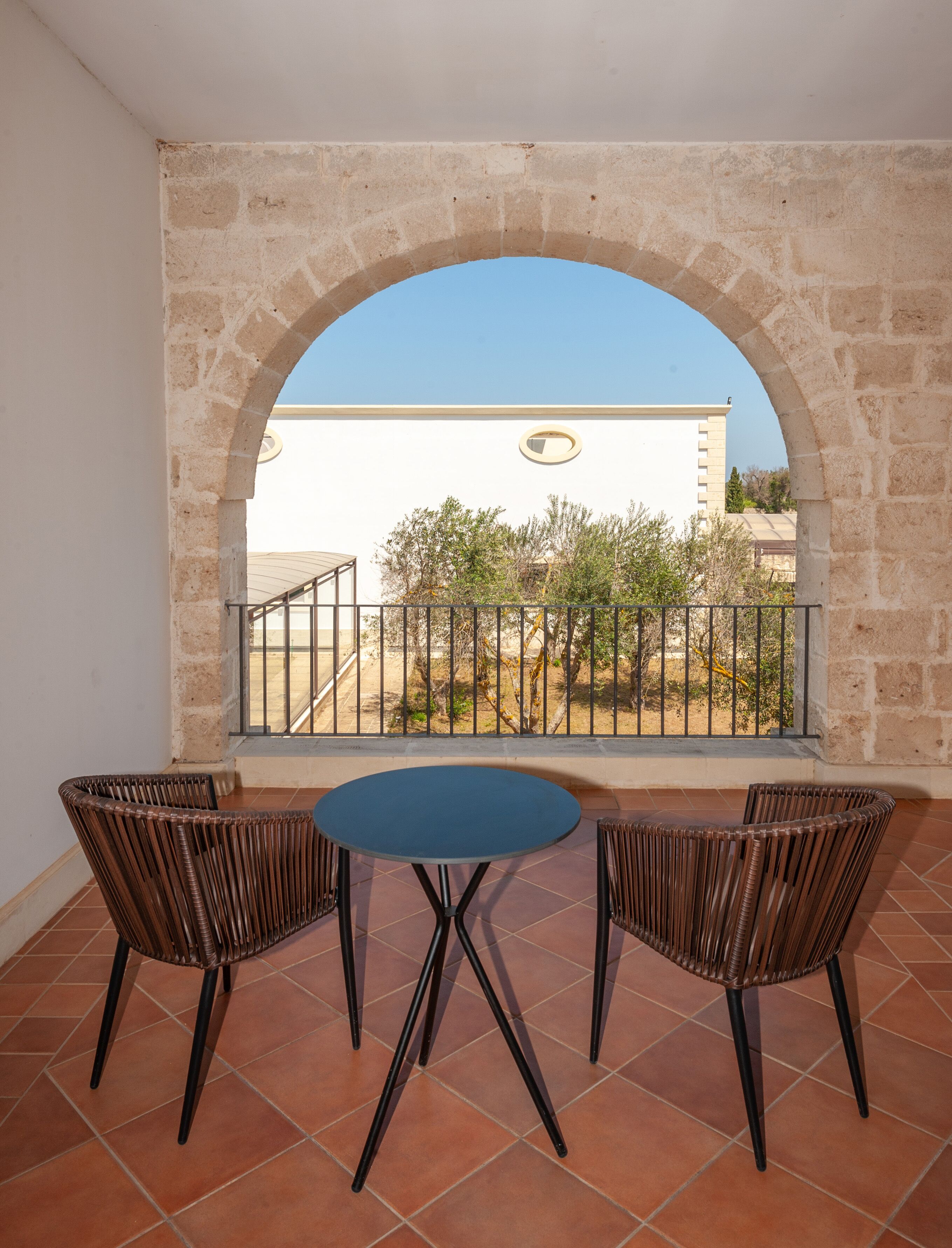 A balcony with a stone arch, two wicker chairs, and a small round table.