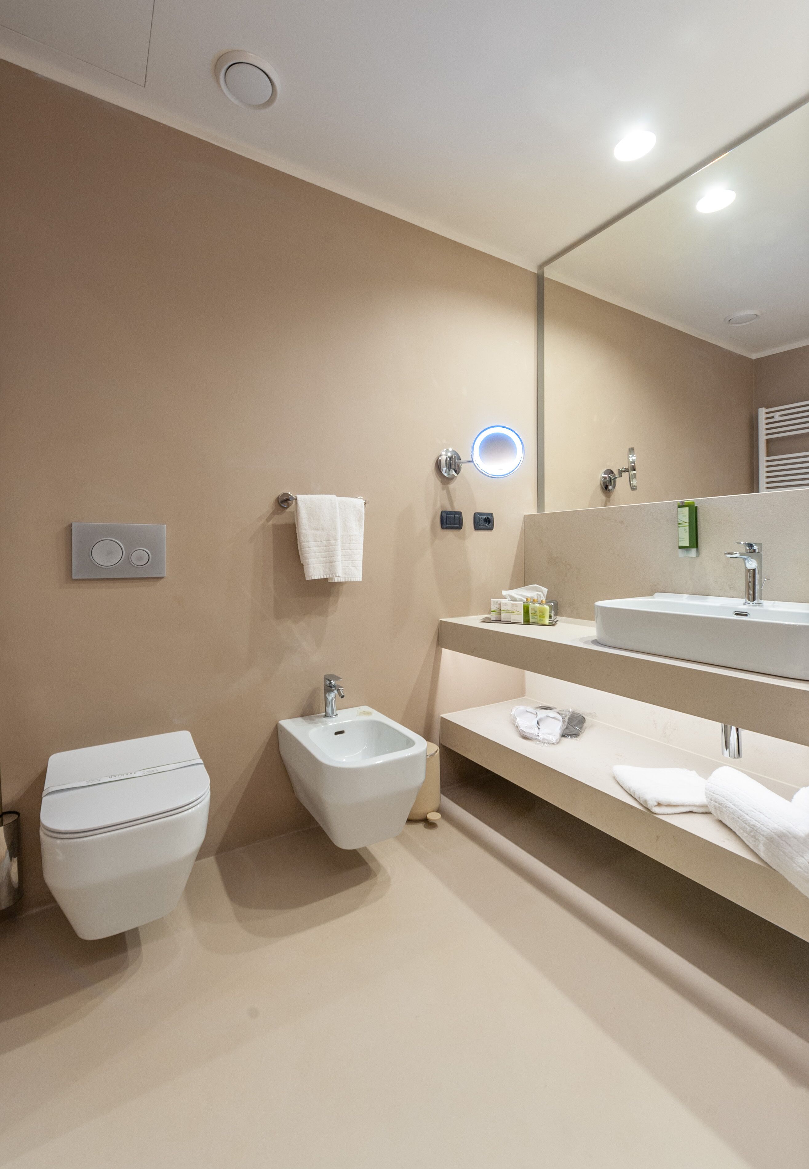 Un baño moderno con inodoro, bidé y un espejo grande sobre un lavamanos.