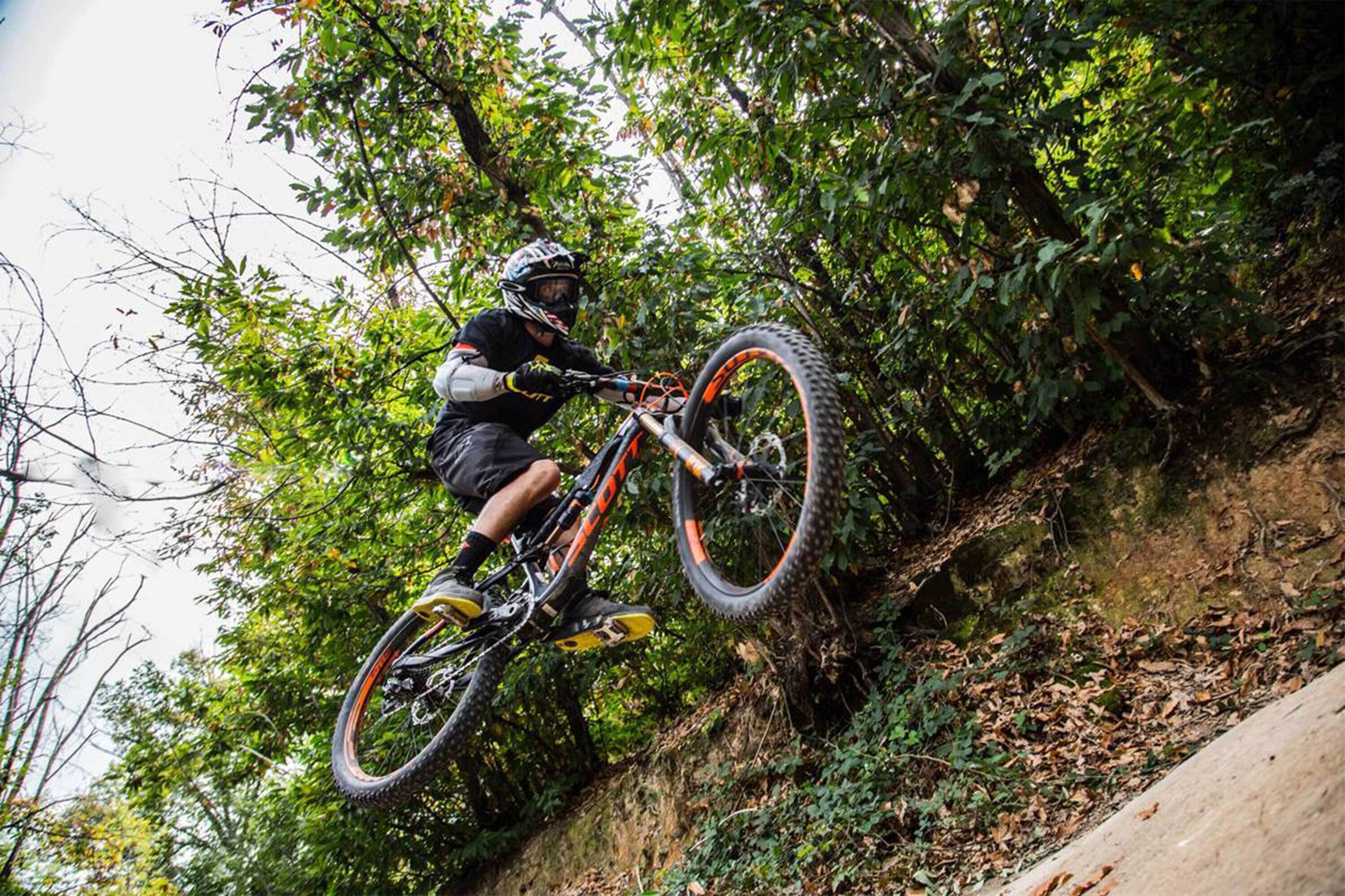 A mountain biker on a trail with dense foliage and a rocky terrain.