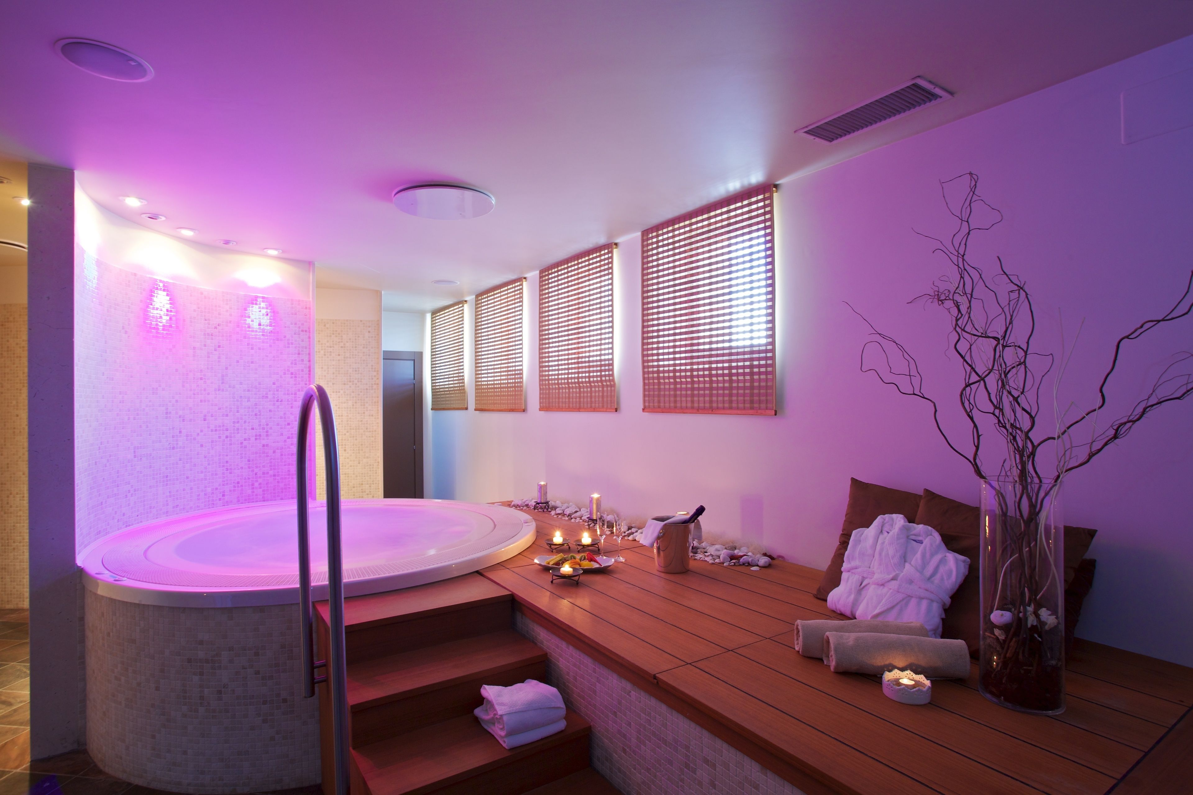 A spa room with a hot tub, wooden seating, candles, and a vase with branches.