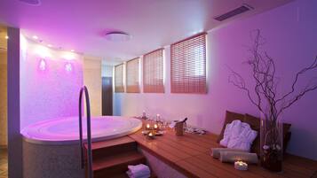 A spa room with a hot tub, wooden seating, candles, and a vase with branches.