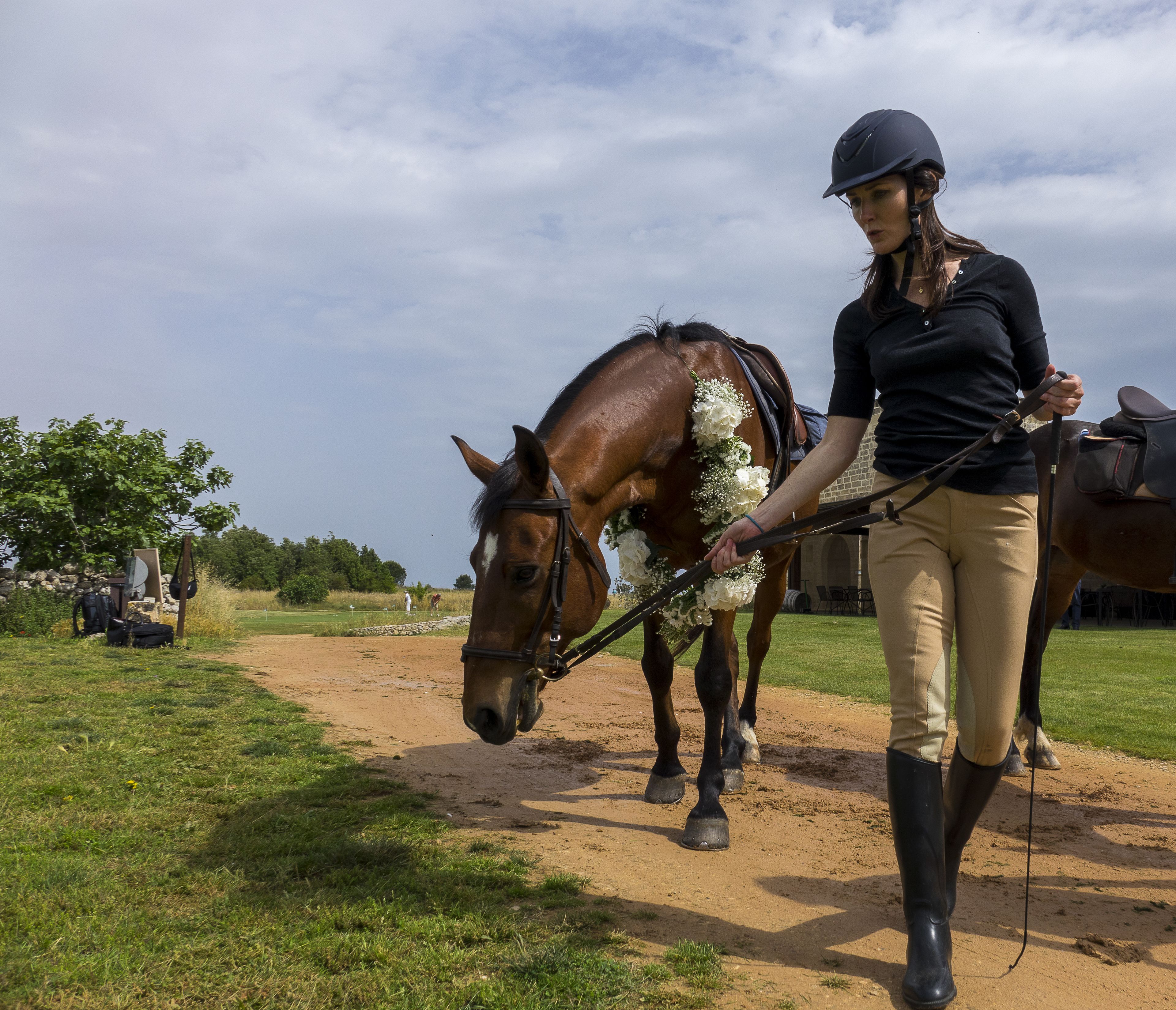 A person leading a horse with a floral arrangement on its head.
