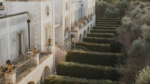 A historic building with a series of arches and balconies overlooking a meticulously maintained hedge garden. - Acaya Golf Resort & SPA (Vernole)