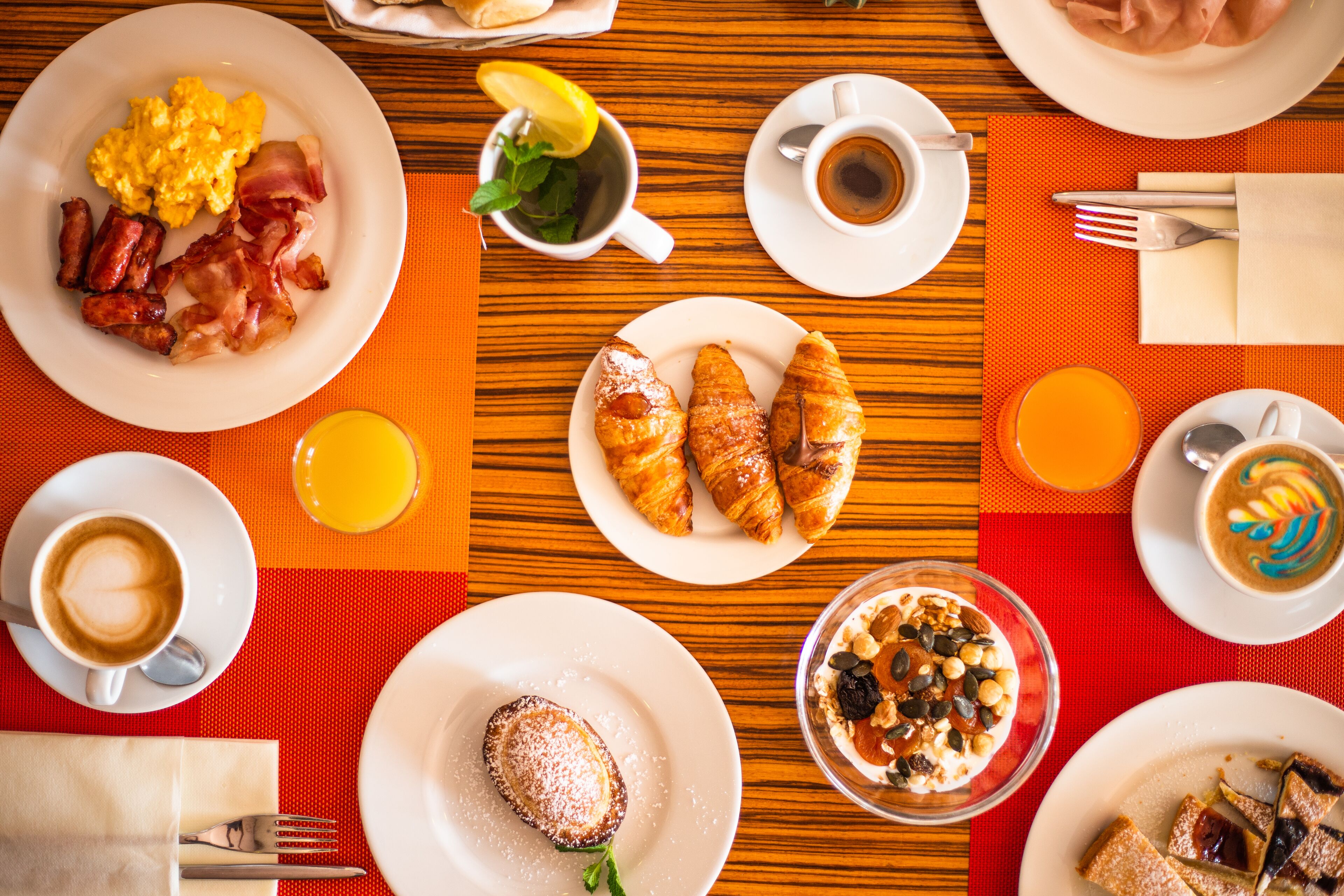Une table dressée pour le petit-déjeuner, avec des assiettes d’œufs, de bacon, de croissants et de viennoiseries, ainsi que des tasses de café et des verres de jus de fruits.
