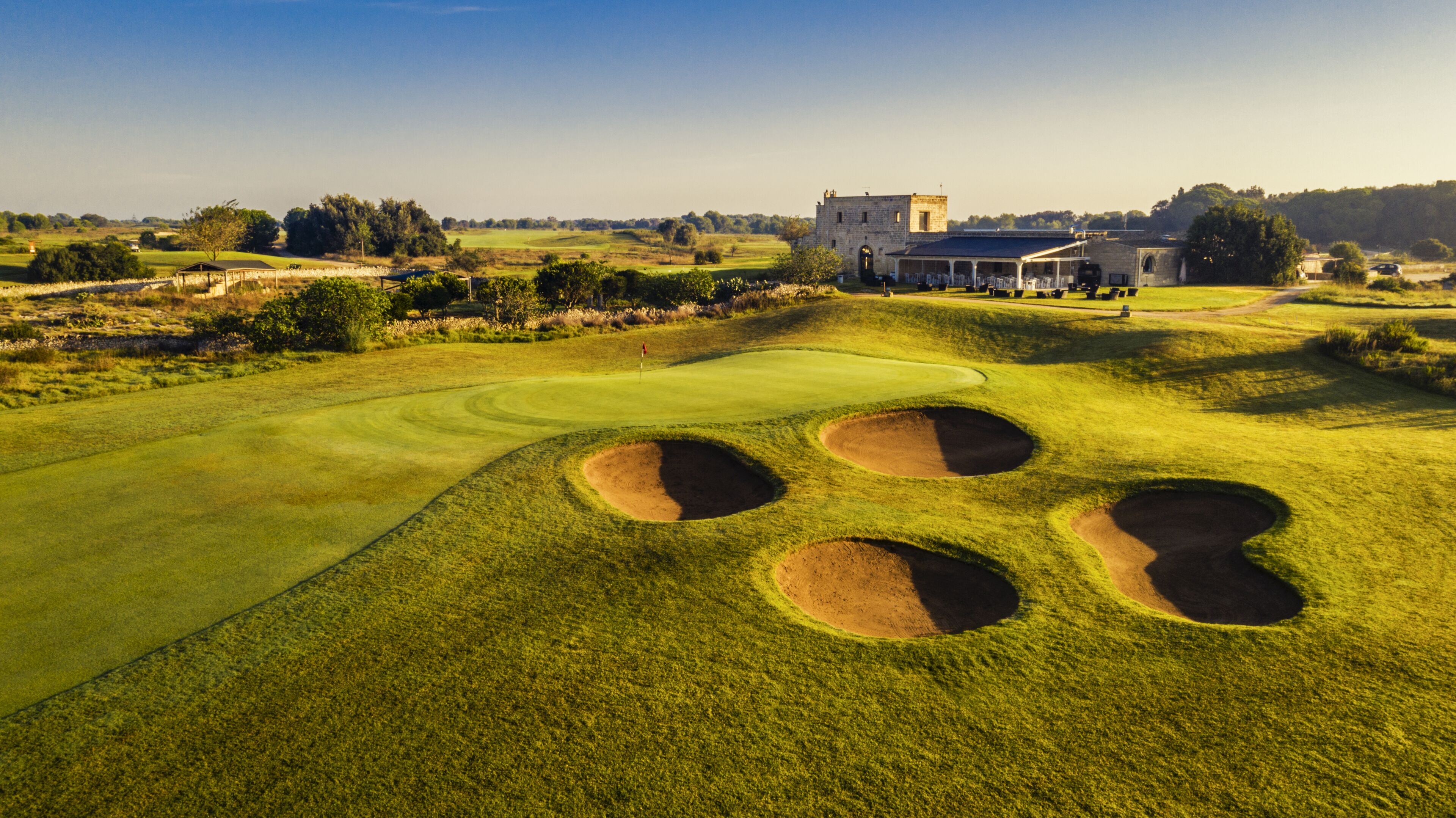 A golf course with bunkers, a clubhouse, and a stone building in the background.