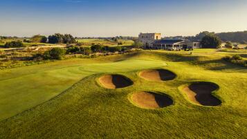 Ein Golfplatz mit Bunkern, einem Clubhaus und einem Steinhaus im Hintergrund.