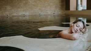 A person lying in a spa bath with a wooden floor and a brick wall in the background. - Acaya Golf Resort & SPA (Vernole)