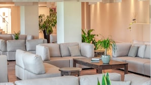 A modern living room with a sectional sofa, a coffee table, and potted plants. - Acaya Golf Resort & SPA (Vernole)