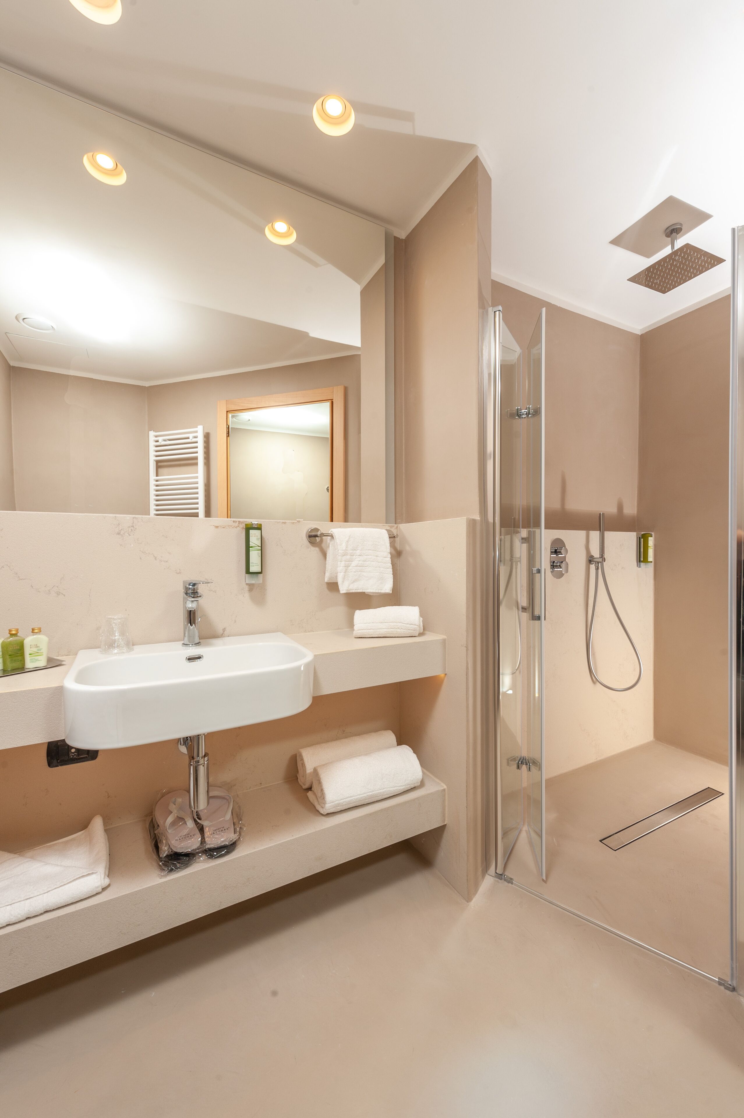 Ein modernes Badezimmer mit einer Glastrennwand zur Dusche, einem großen Spiegel und einem weißen Waschbecken.