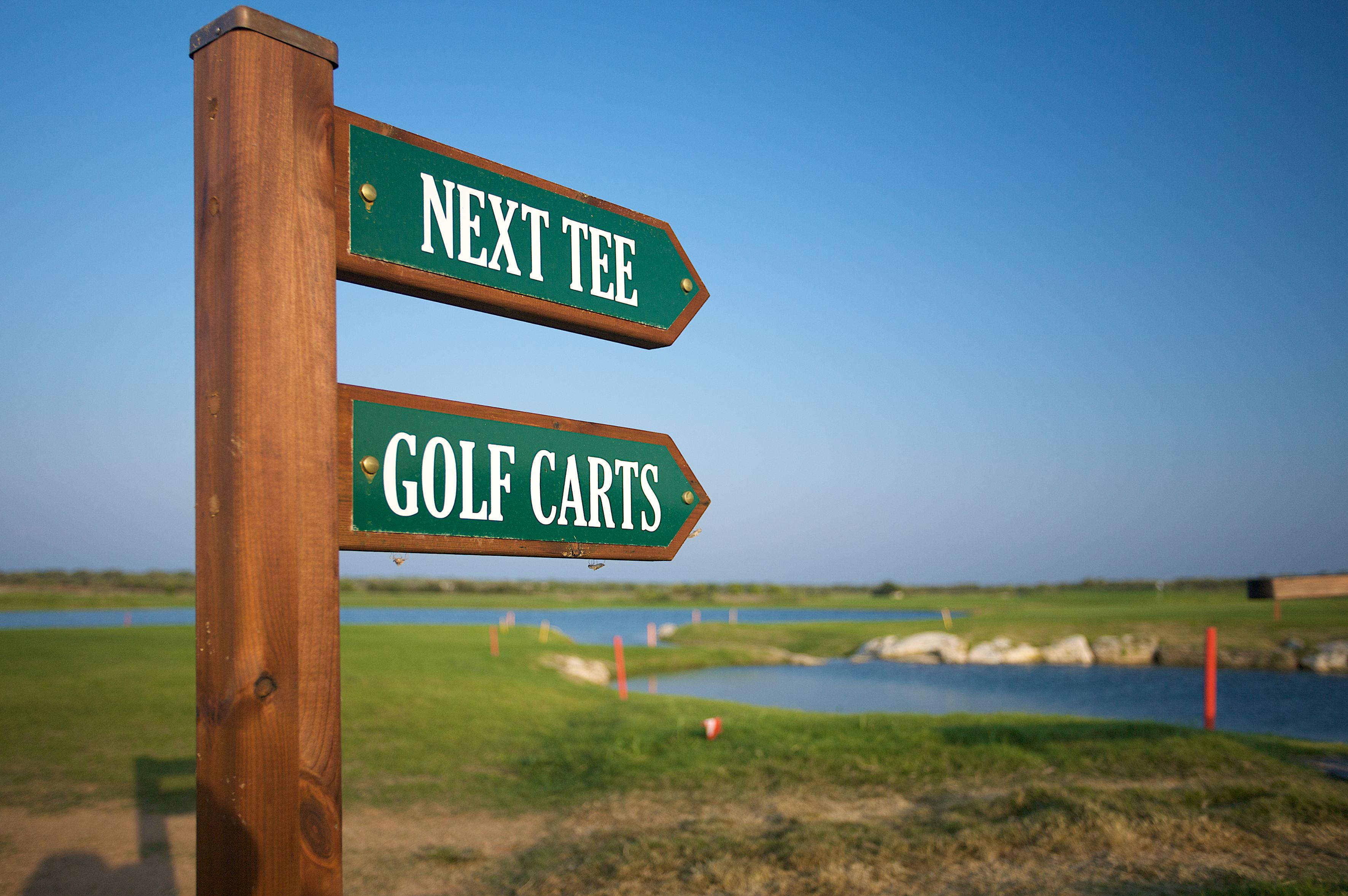 Un cartello in legno con frecce direzionali che indicano 'Next Tee' e 'Golf Carts'.