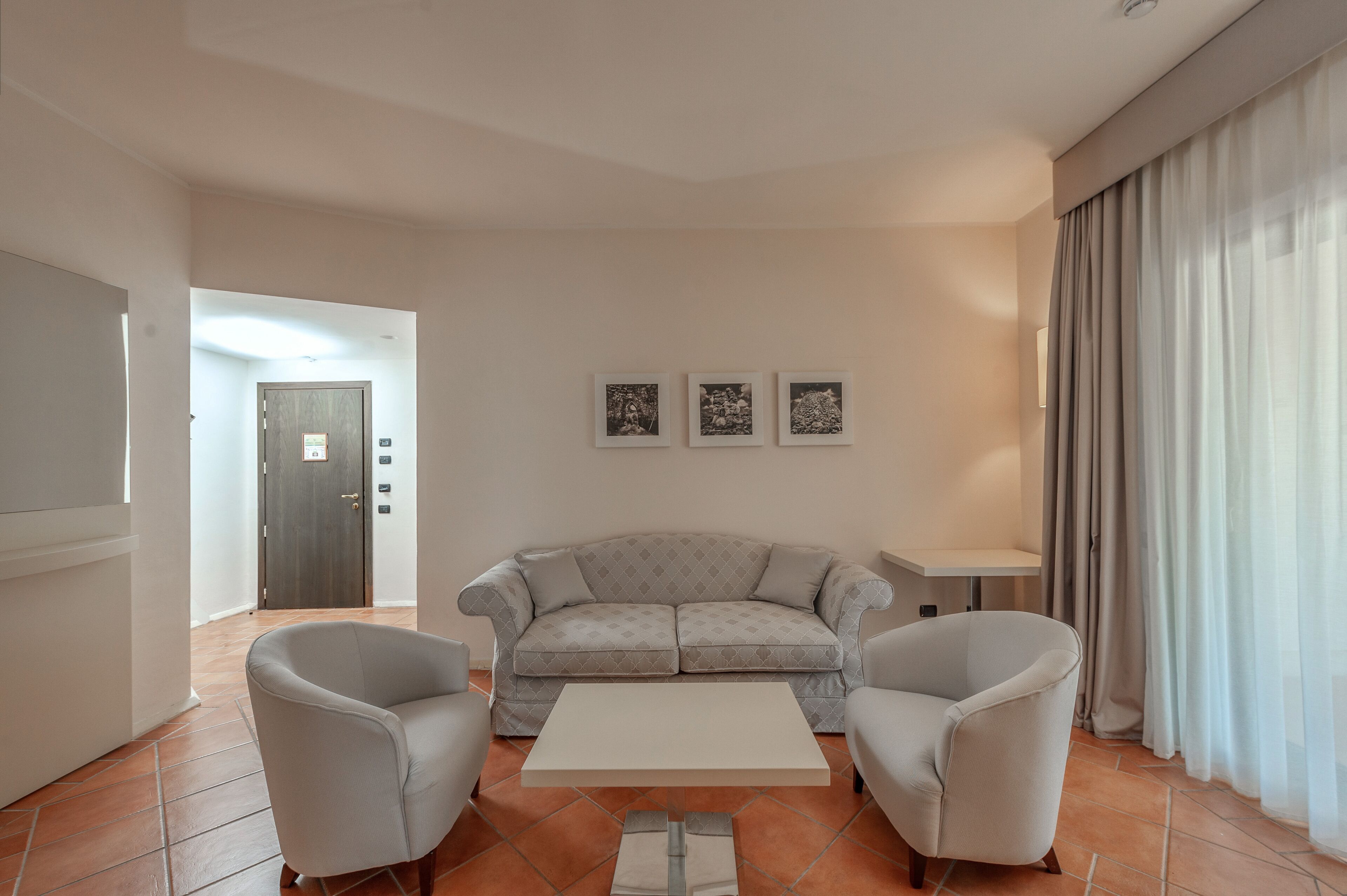 A living room with a grey sofa, two armchairs, a coffee table, and a door in the background.
