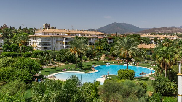 A resort with a large swimming pool surrounded by lush greenery and palm trees, with multiple buildings in the background. - Puerto Banús Luxury Penthouse (Marbella)