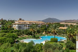 Un complexe hôtelier doté d’une grande piscine entourée d’une végétation luxuriante et de palmiers, avec plusieurs bâtiments en arrière-plan.