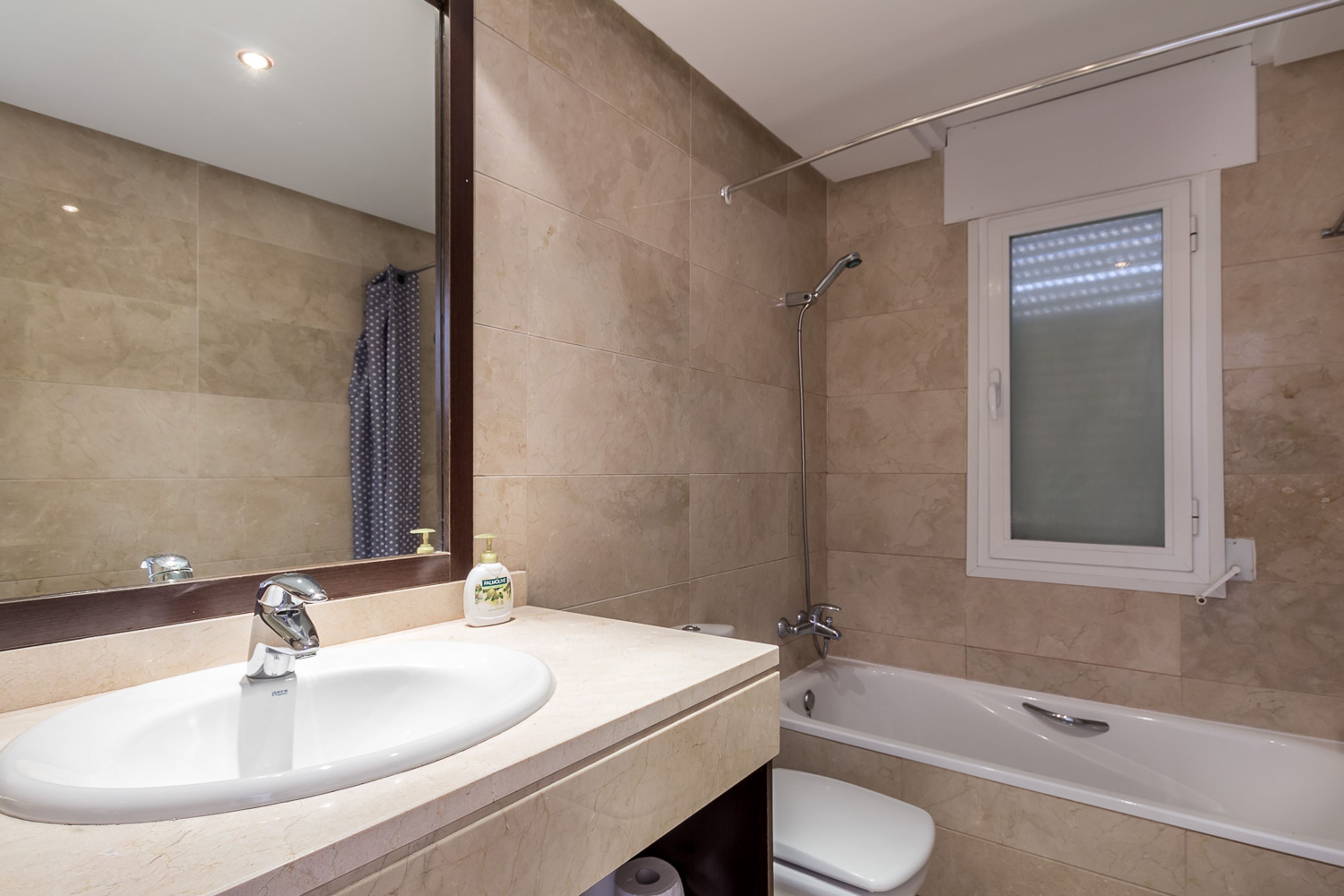 A modern bathroom with a large mirror, a sink, a toilet, and a bathtub.