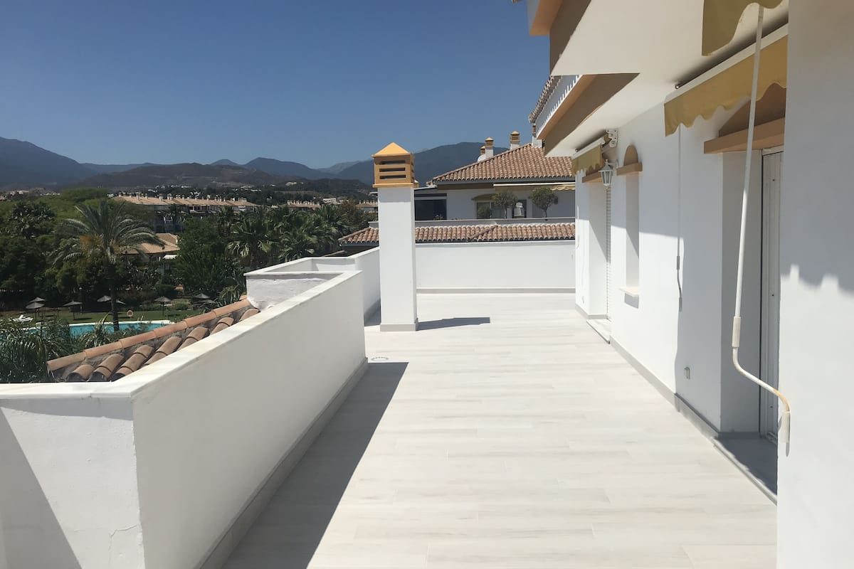 Un balcon offrant une vue dégagée sur une piscine, des montagnes et une ville située au loin.