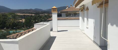 A balcony with a clear view of a swimming pool, mountains, and a distant town.
