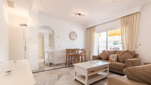 A modern living room with a white coffee table, beige sofa, and a dining area with wooden chairs and a white table. - Puerto Banús Luxury Penthouse (Marbella)