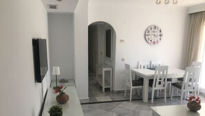 A modern dining area with white furniture, a clock on the wall, and a vase with flowers on the table. - Puerto Banús Luxury Penthouse (Marbella)