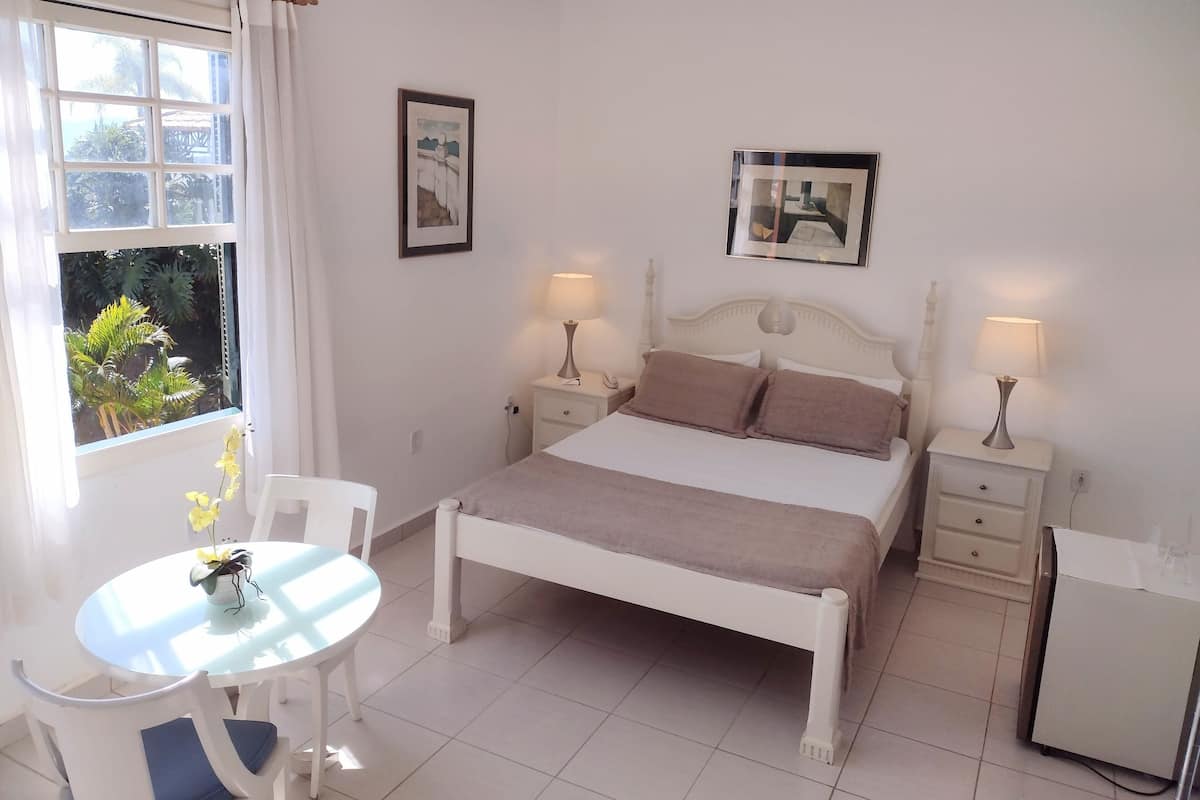A neatly arranged bedroom with a bed, bedside tables, a small table with chairs, and a window with curtains.