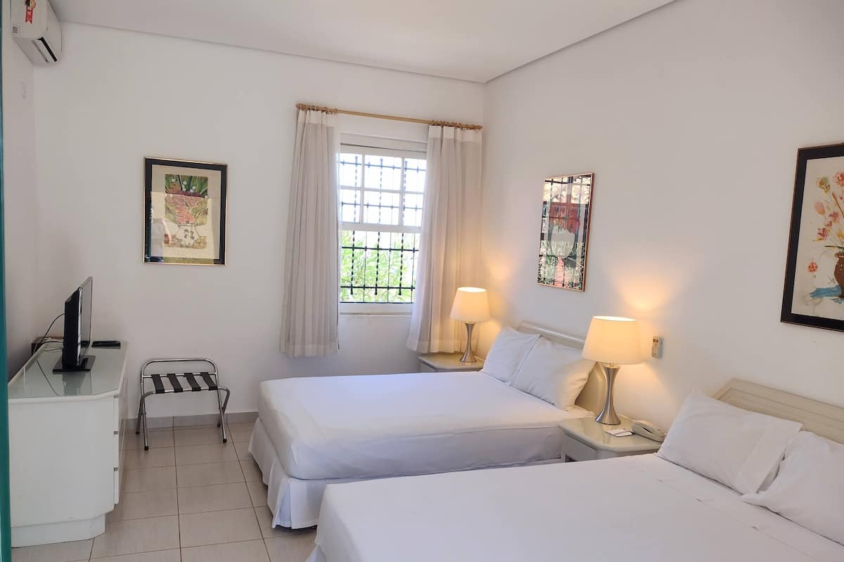 A hotel room with two beds, a desk with a computer, a window with curtains, and wall art.