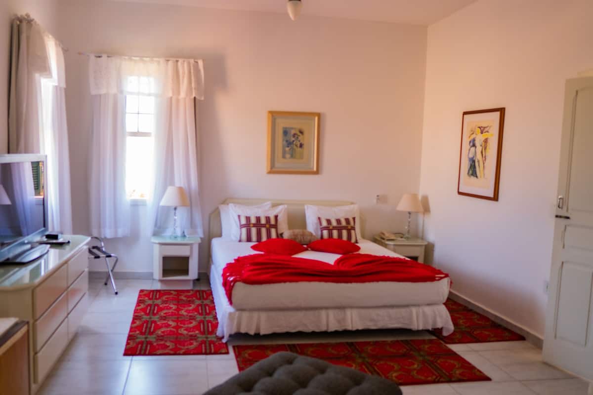 A bedroom with a bed, a TV, a bedside table, a lamp, and a window with curtains.