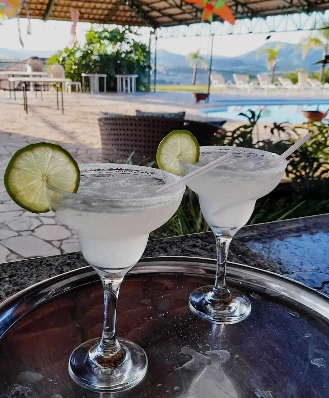 Two margaritas on a metal tray with a pool and outdoor seating in the background.