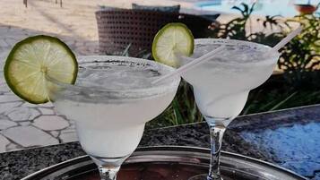 Two margaritas on a metal tray with a pool and outdoor seating in the background.