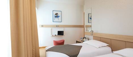 Habitación de hotel con dos camas, un escritorio con computadora, un espejo y un cuadro en la pared.